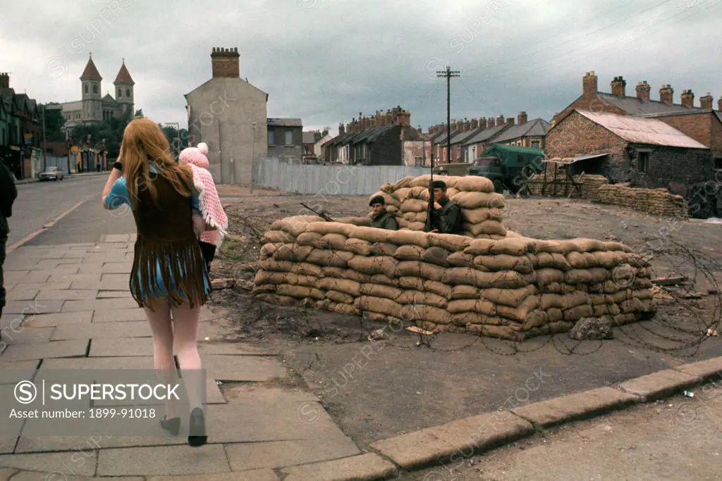A woman with a newborn in her arms passes a road block. Belfast. (Northern Ireland), July 1970.