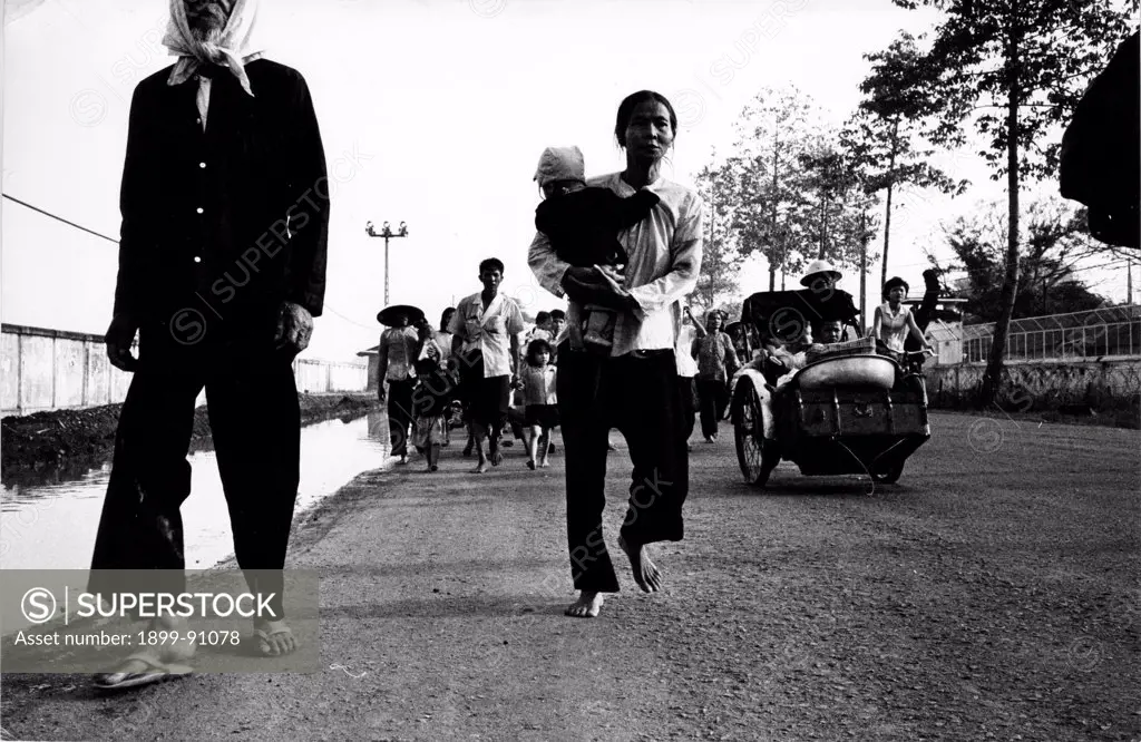 Some refugees taking flight across a Y-bridge. Some are on foot, some other are on a bike or on a tricycle. In the close-up a woman with a child in her arms. War in Vietnam (1960-1975). Saigon (Vietnam), May 1968.