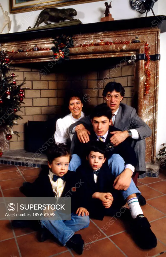 The leader of the Northern League party (Lega Nord), Umberto Bossi, crouching in front of the fireplace in his house in Gemonio, next to his eldest son Riccardo, his second wife Manuela Marrone and their two children. Gemonio (VA), Italy, the '90s.