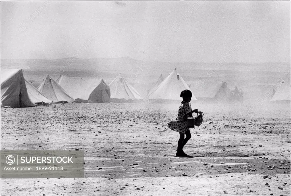 A young girl is walking in the desert. Behind her, the tents of the refugee camp of Wadi Dlails, one month after the Six-Day War. Jordan, July 1967.