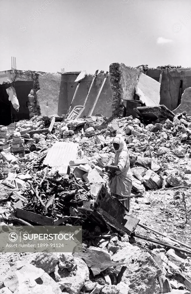 A woman among the ruins of some destroyed houses of the Palestinian town of Qalqilya, after the Israeli attack during the Arab-Israeli War, known as Six-Day War. 1967.