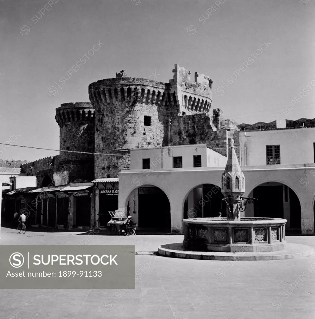Panorama of Hippocrates Place: a corner of the bazar, with Saint Catherine's gate and a nice fountain. Rhodes (Greece), June 1959.