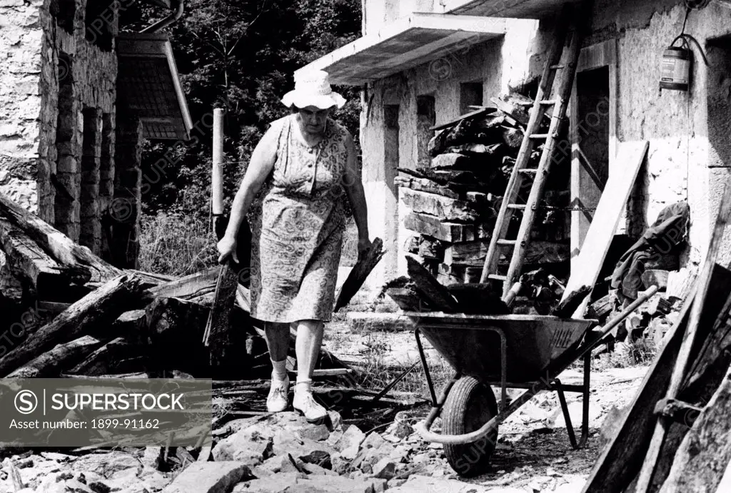 A woman collects the rubble of the remains of her house after the earthquake  of May 6th, 1976 hits  Friuli; the woman has two pieces of wood in her hand. Around her everything collapsed. Flaipano (UD), Italy, August 1977.