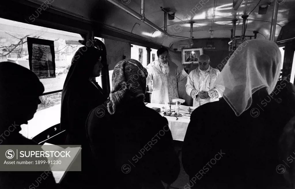 Because of winter chill and earthquake, which crushed down the village church in May, the priest is serving Mass in a bus donated by the Genoa municipal tram service company; in the driver's cab, father Claudio Bevilacqua arranged an altar and removed the seats to leave more room for the believers. Montenars (UD), Italy, December 1976.