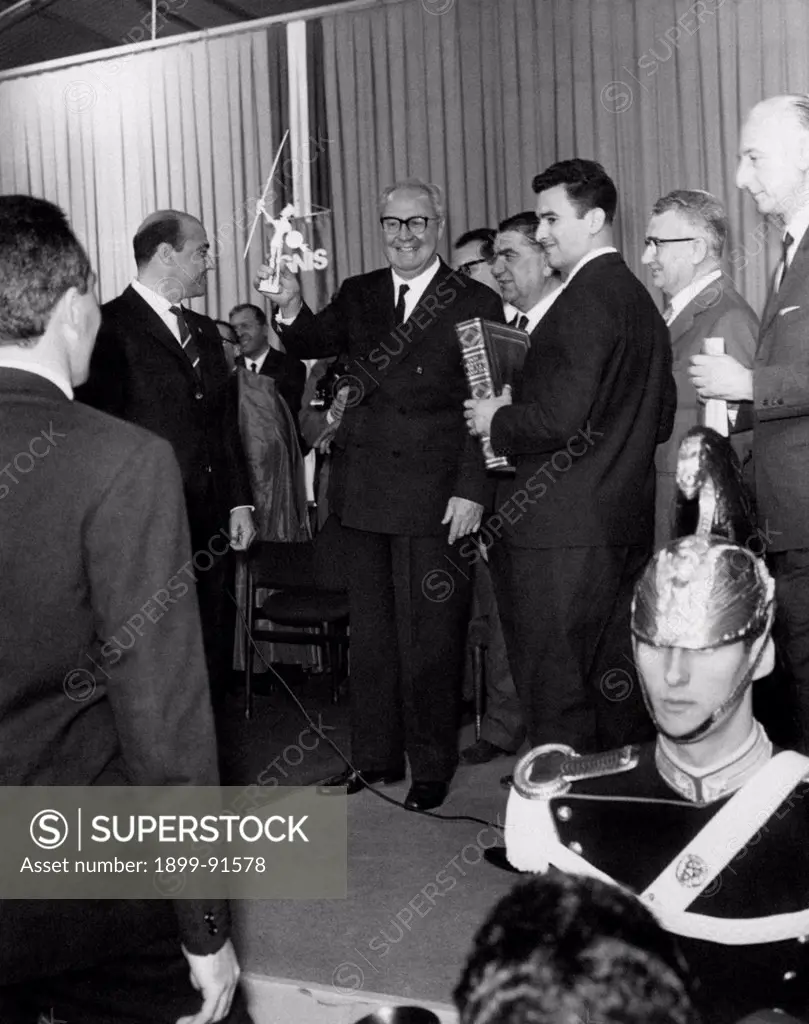 President of the Italian Republic Giuseppe Saragat smiling and raising the symbol of the Ignis household appliances' factory. Giuseppe Saragat visited the Ignis factory in Cassinetta di Biandronno with the Knight of Merit for Labour and President of the factory Giovanni Borghi. Biandronno, October 1965