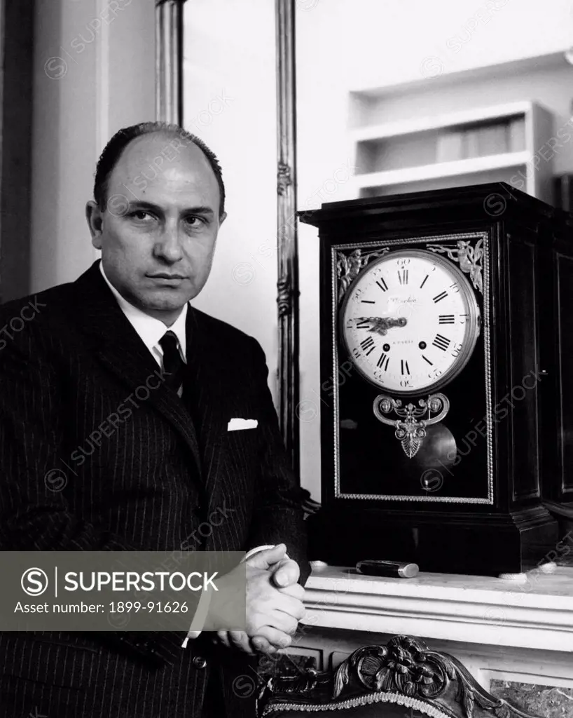 Italian lawyer and Christian Democrat deputy Danilo De' Cocci photographed beside a pendulum-clock. 1963