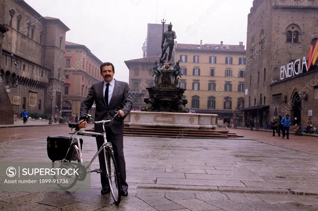 Italian politician and Mayor of Bologna Renzo Imbeni in Piazza Nettuno with his bicycle. In the background one can see the Fountain of Neptune made by Giambologna (Jean de Boulogne). Bologna, 1980s