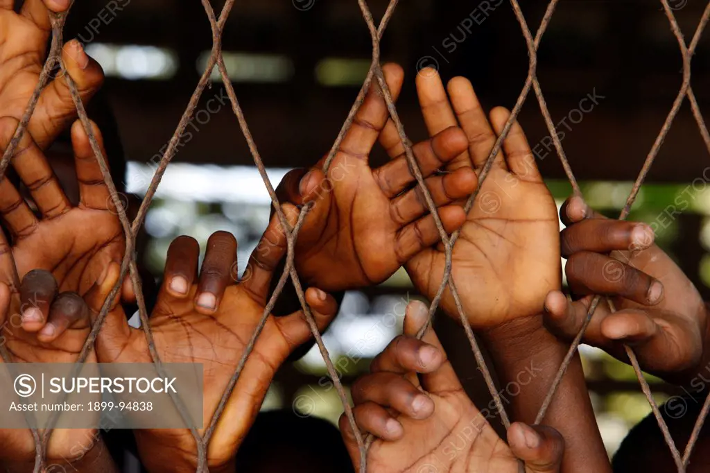 African boys' hands behind wire mesh, Lome, Togo.,02/11/2009