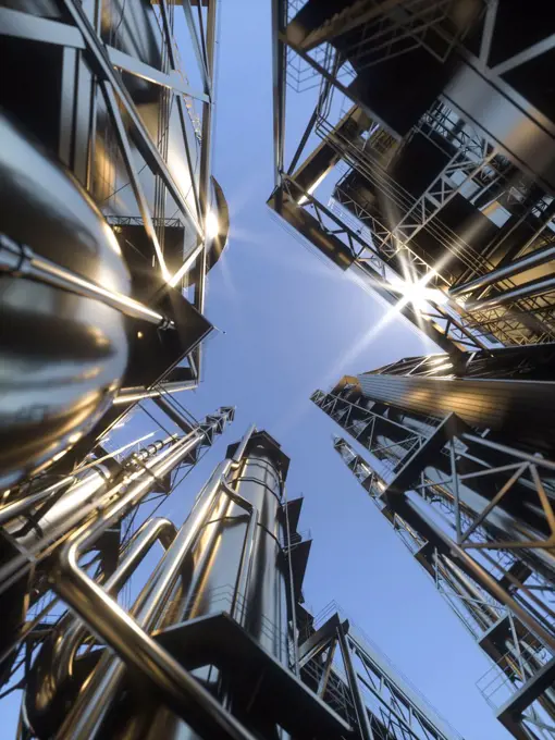 Looking up on a clear day at an oil refinery with large reflective chimney stacks in the sun 3D Rendering