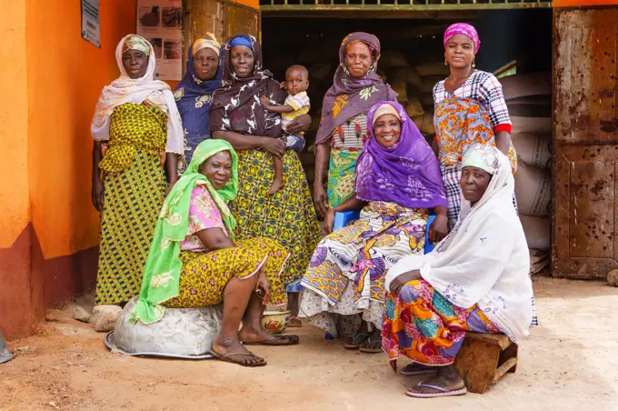 These West African women wearing traditional colorful dress pose for the camera in their village ca. 21 February 2018.