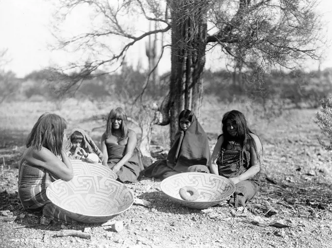 Maricopa group, Arizona. Four women and a child seated on ground with three large basket trays. 