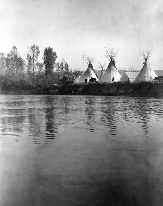 Edward S. Curtis Native American Indians - Crow encampment with tipis, tents, wagons, horses and men as seen from the distant shore of the river ca. 1908. 