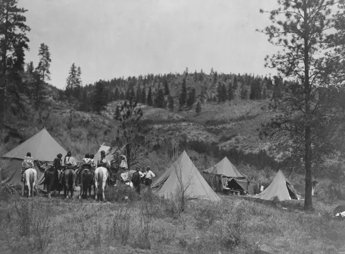 Edward S. Curtis Native American Indians - Five tents erected in a clearing, Edward S. Curtis in center, Spokane men and women on horseback on the left ca. 1910. 