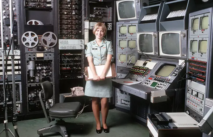 A female U.S. Army audiovisual technician stands beside a videotape editing console. 