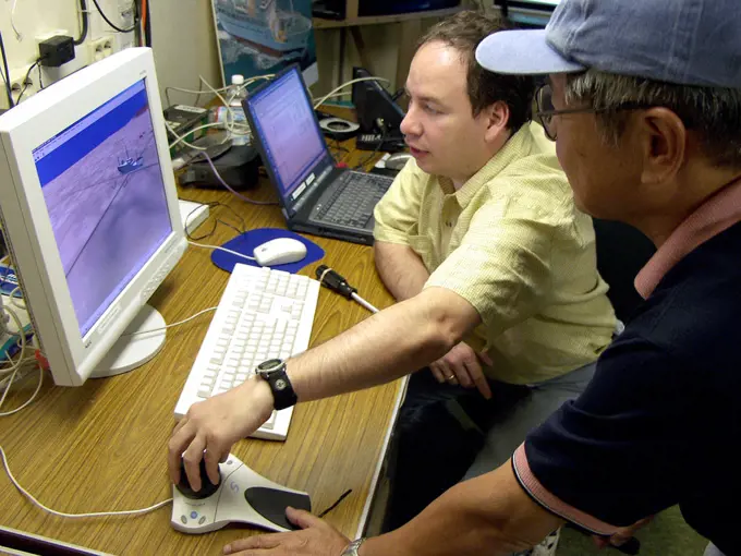 Mr. Hiroyasu Takemoto from the Japanese Government, National Maritime Research Institute, Structural Mechanics Division, observes as Mr. Juan Santamaria (right), of XYZ Solutions demonstrates a computer animated model on the computer, onboard the Bahamian, Multi-purpose Diving Support Vessel (DSV) 'Rockwater 2', during Ehime Maru recovery operations.. 