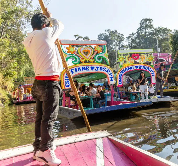 Popular tourist attraction people boating on colorful barges on canal at Xochimiloco, Mexico City, Mexico, trajinero punting barge.