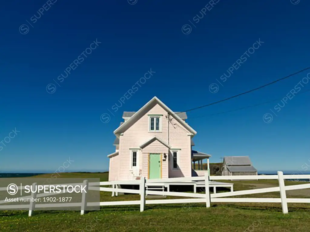 Canada Quebec Gaspesie Riviere-la-Madeleine pink house and with white fence against a blue sky