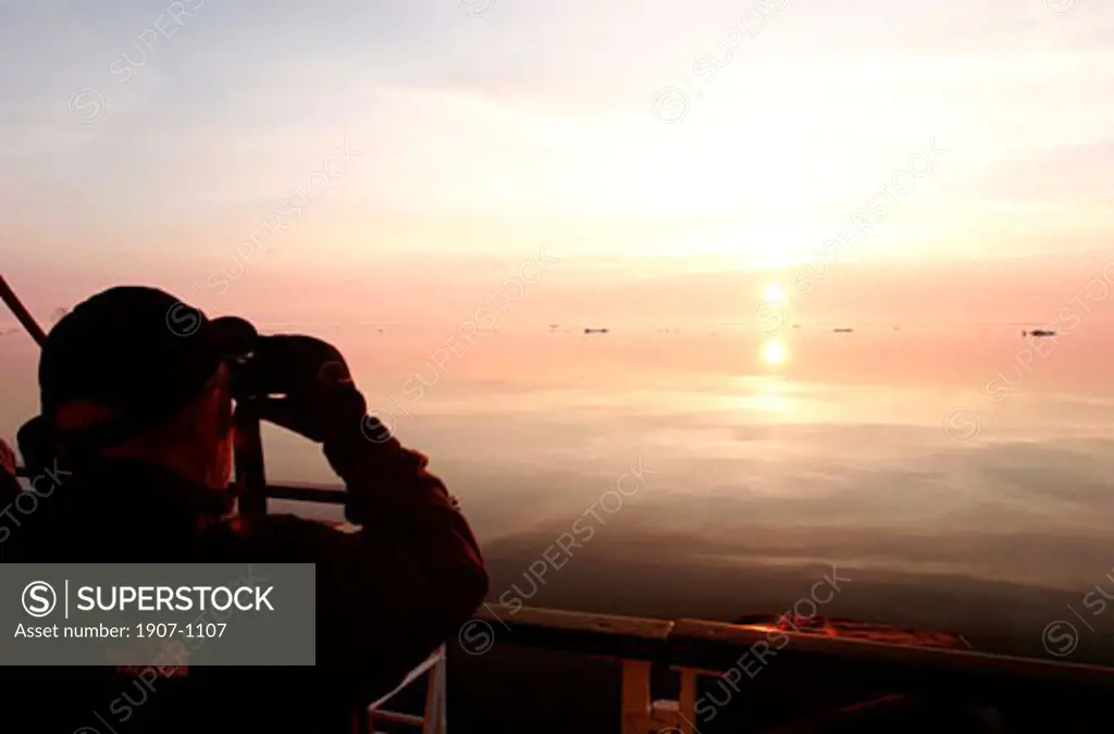 The Lyubov Orlova during navigation beyonf the polar circle  around Baffin island  a man watching the midnight sun