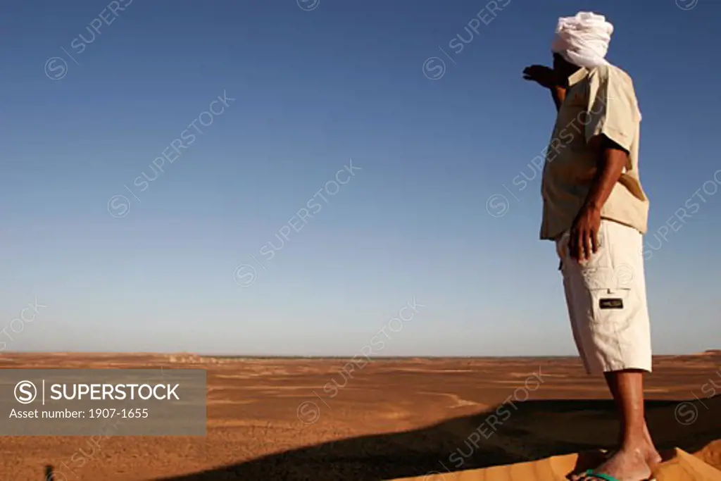 A man on the crest of a dune  in the Dongola desert  watching  in the far  the Old Dongola oblong pyramids