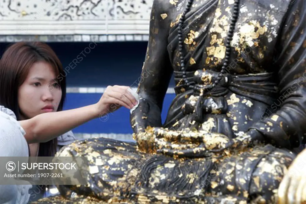 A woman is applying a gold sheet on a Buddha statue in Sop Ruak