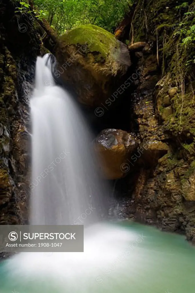 Scenic shot of a small Costa Rica tropical waterfall surrounded by trees and rocks covered in green moss