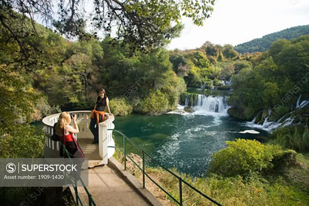 Girl taking photograph of her friend overlooking the Skradinski Buk waterfalls on the River Krka in autumn sunshine Krka National Park Dalmatia Croatia Europe