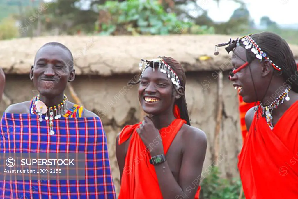 Masai warriors wear traditional red blankets in the Masai Mara National Nature Reserve Kenya East Africa Village huts are made from sticks and cow dung
