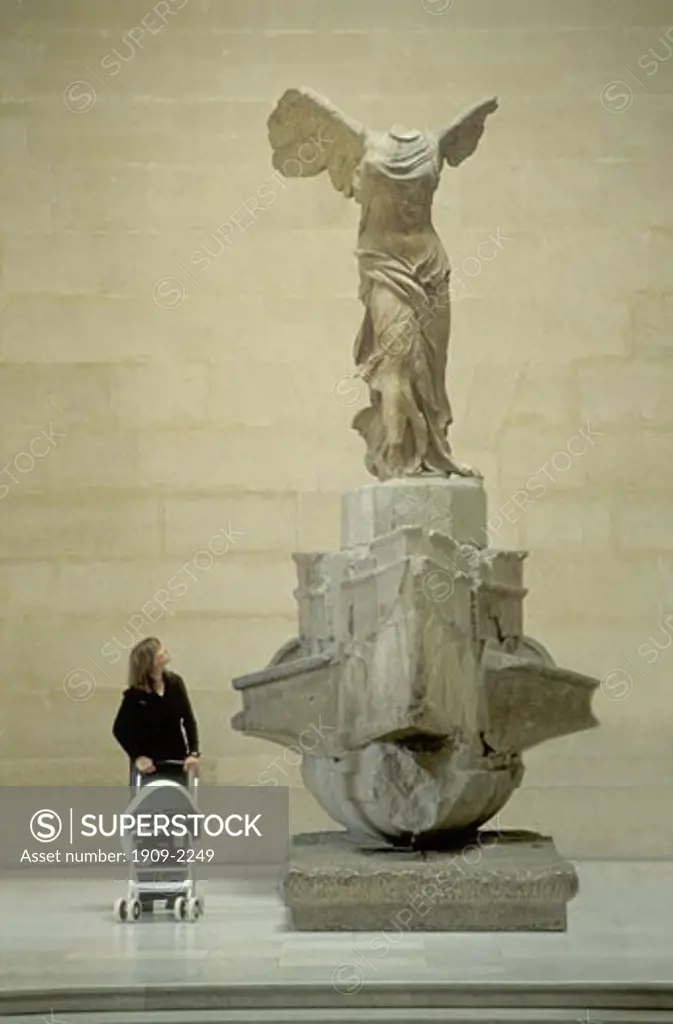 Modern woman contemplates the 2nd Century BC Winged Victory of Samothrace statue in the Louvre Museum Palais du Louvre Paris France Europe