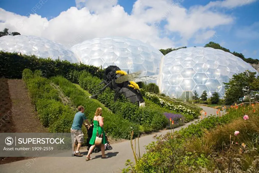 Young couple pushing buggy along path at Eden Project in summer sun St Austell Cornwall England UK United Kingdom GB Great Britain British Isles Europe EU