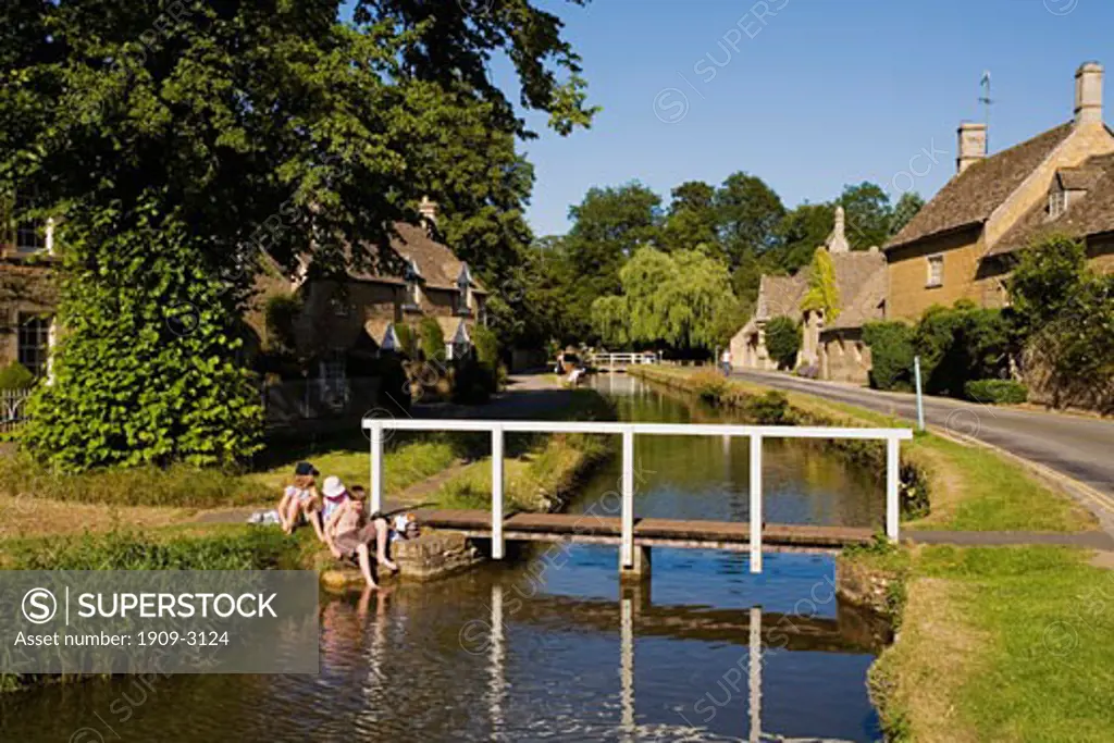 Ancient english traditional cottages in summer sunshine with blue sky and pedestrian footbridge over the River Windrush at the village of Lower Slaughter Gloucestershire Cotswolds England United Kingdom UK Great Britain GB British Isles Europe EU