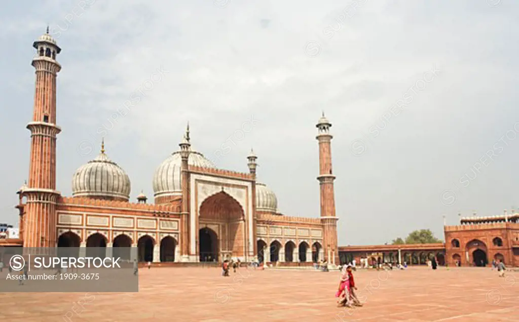 Woman in sari walks across the main courtyard in front of minarets and domes of the Jami Masjid Mosque built in 1656 by Emperor Shah Jahan in Delhi Uttar Pradesh Northern India Asia