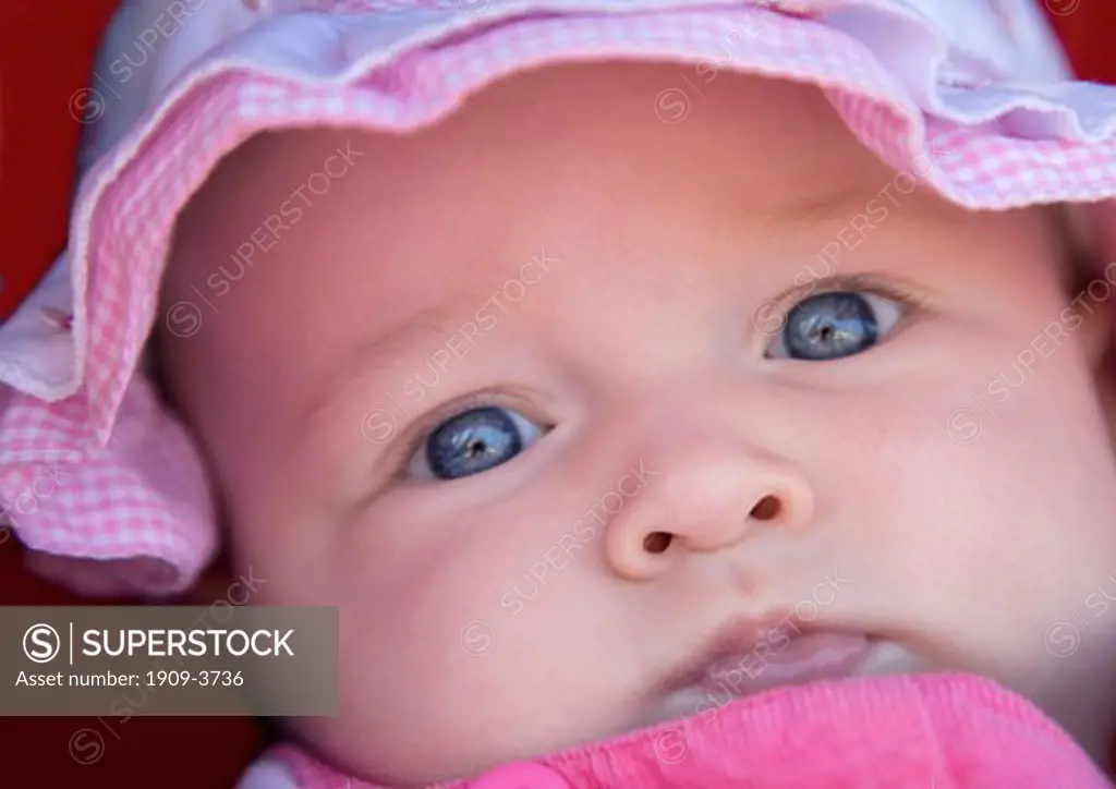 Beautiful 6 month old female girl infant baby toddler in pink sunhat hat with blue eyes close up closeup close-up face