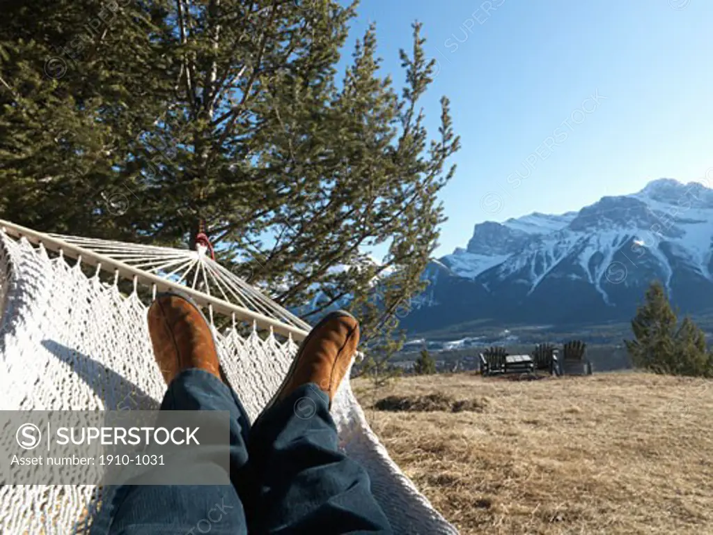Detail of mans legs while lying in hammock  alpine meadow and Three Sisters Mountain behind  above Canmore  Canada  Alberta