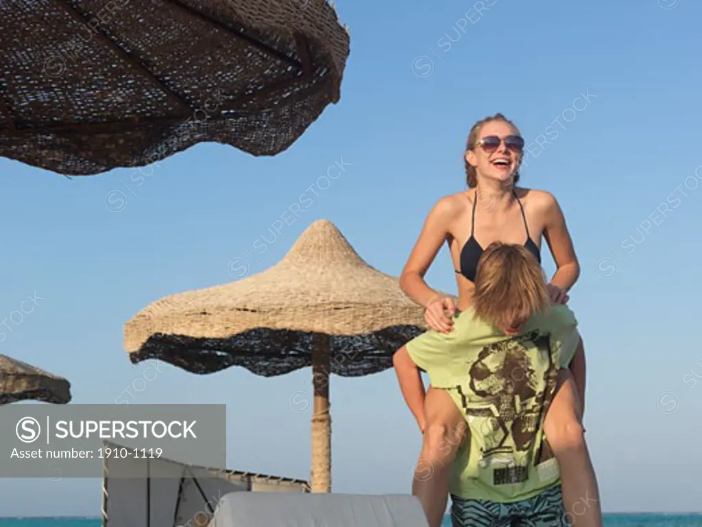 Teenage kids piggyback below palapas  on beach  Egypt  Red Sea Riviera  Marsa Alam