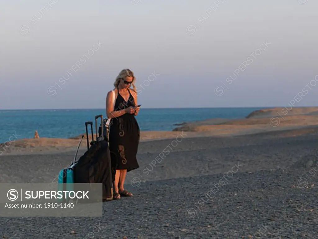 Woman 40s dials mobile phone while standing with luggage  in Sahara Desert  Red Sea below  Egypt  Red Sea Riviera  Marsa Alam