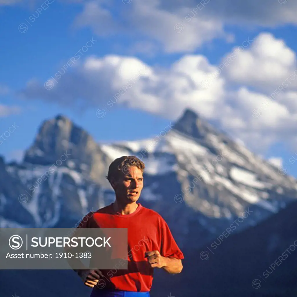 Man 30 yrs running up mountain slope Three Sisters Mountain behind Canmore CANADA Alberta