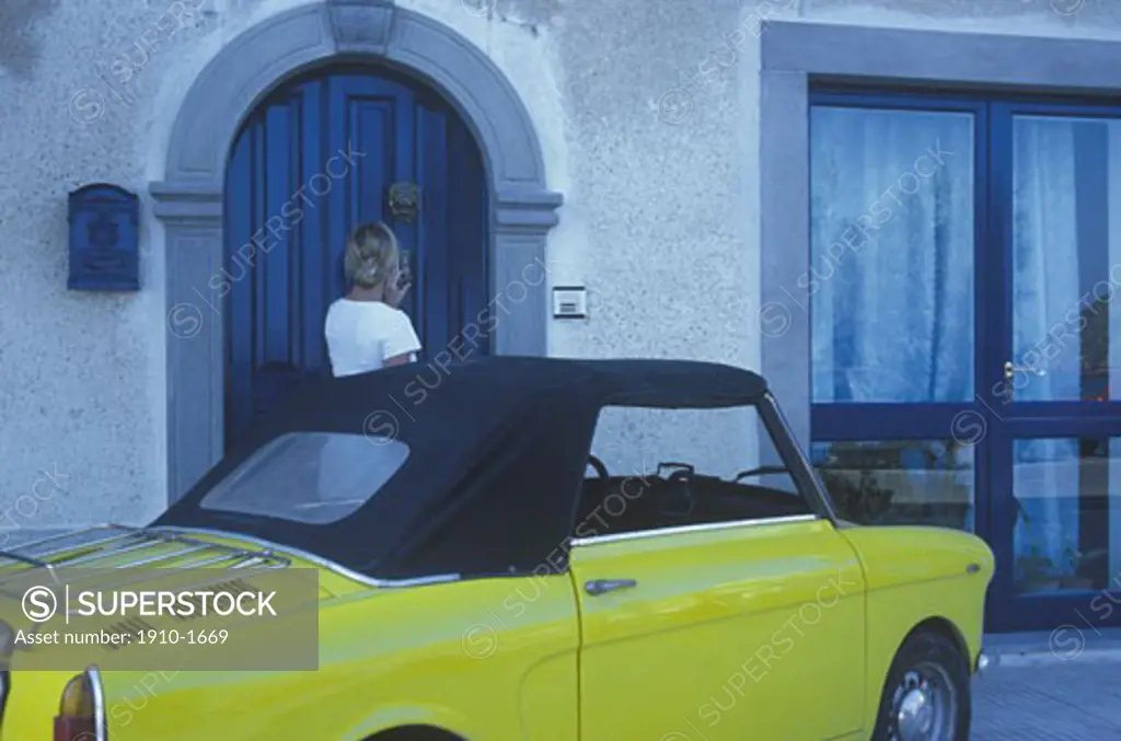 Woman knocking on door beside vintage Fiat car Lipari Lipari is the largest of a chain of seven islands in a volcanic archipelago that straddles the gap between Vesuvius and Etna ITALY Aeolian Islands Lipari