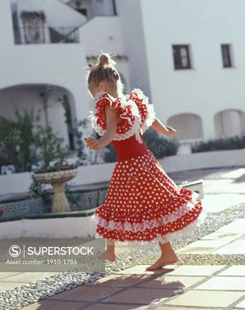 Young girl 7 in flamingo dress dancing in courtyard below whitewashed buildings SPAIN Andalusia