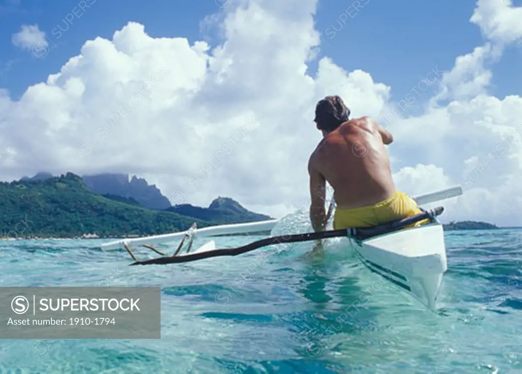 Man paddling outrigger canoe towards distant mountains through gentle waves and clear waters Outrigger canoes are native to the Polynesian islands where they have been used for centuries TAHITI French Polynesia Bora Bora