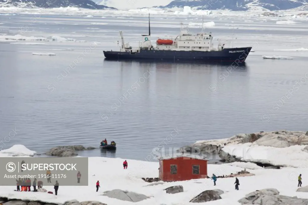 Tourists exploring area around Argentinian scientific research station building, with colony of nesting  Gentoo Penguins (Pygoscelis papua) Antarctica Cuverville Island, Gerlache Strait