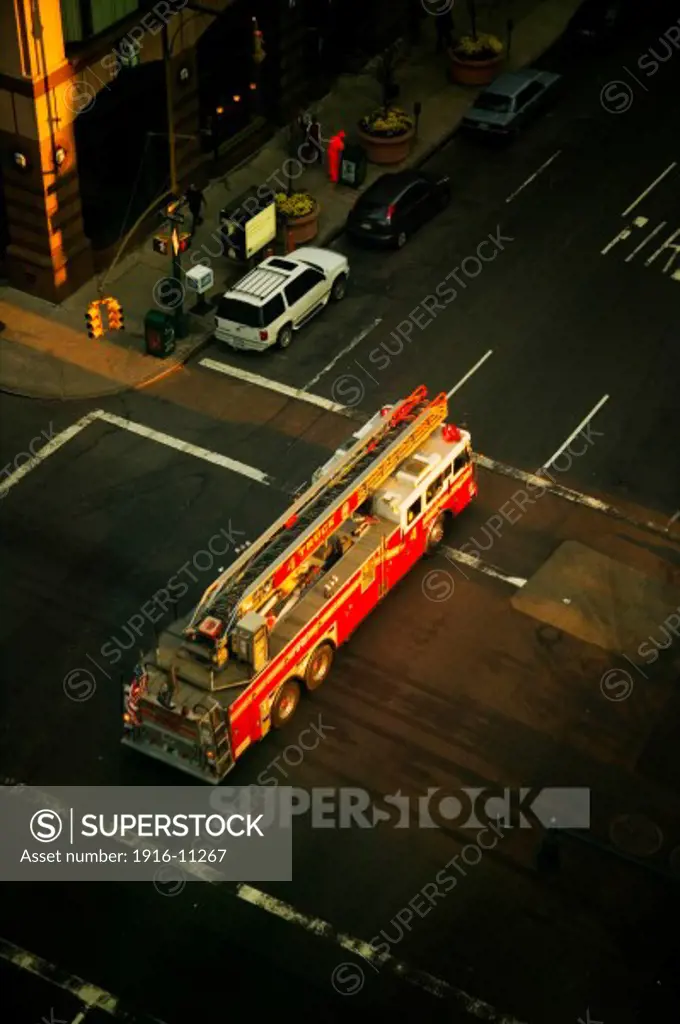 Overhead view of Midtown Manhattan New York Fire Department NYFD Ladder 4 fire truck passes through shaft of early morning sunlight at intersection of West 48 Street and Eighth Avenue on the way to emergency fire call, New York City, NY