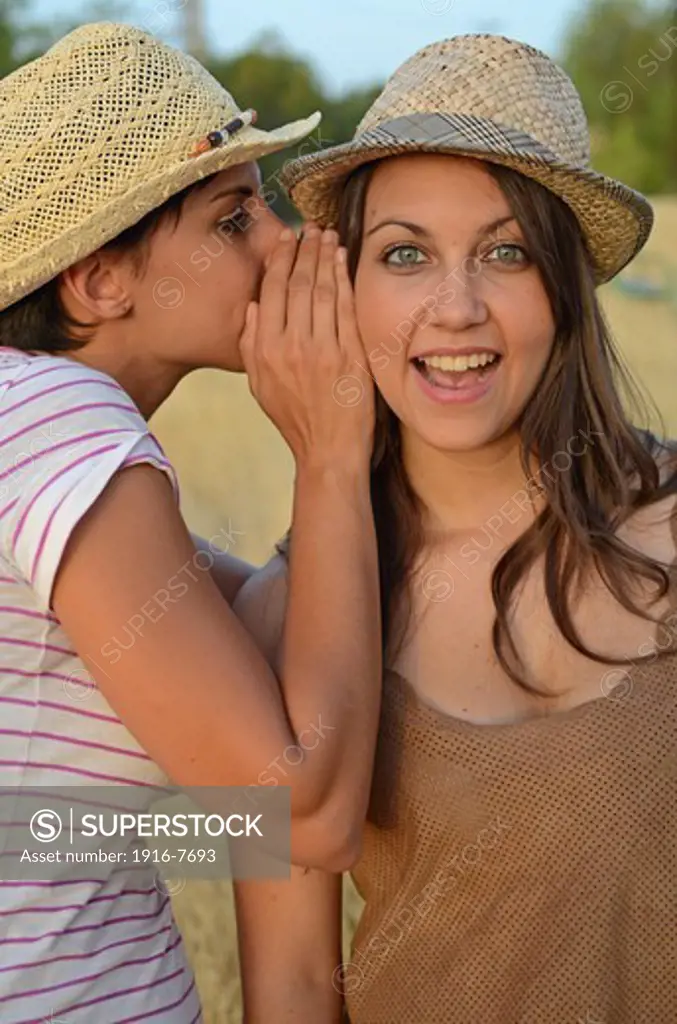 Young woman whispers in friends ear