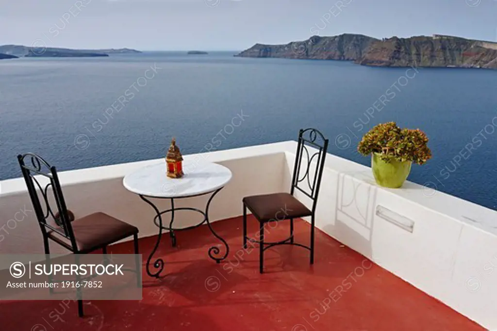 Greece, Santorini, Oia, Chairs and table on balcony, Santorini caldera in background