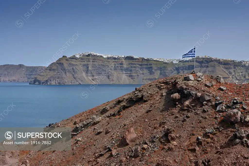 Small hill with the Greek flag and Fira in the background, Nea Kameni, Santorini, Greece