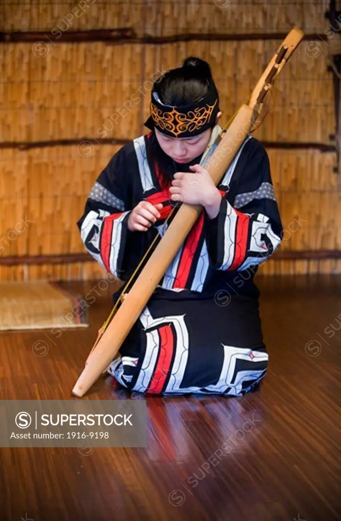 Ainu woman playing a traditional instrument in Ainu village museum,Shiraoi Poroto Kotan,Shiraoi,Hokkaido,Japan