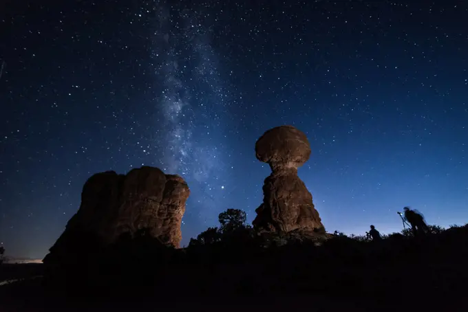 Photographers at dusk taking pictures to the Milky Way behind the Balanced Rock, Arches National Park, USA