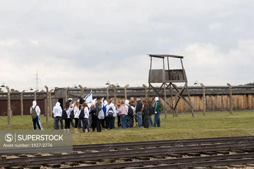 Group of young Israelis carrying Israel flags visit the Birkenau Death Camp with the rail siding that carried the vistims in the foreground and a guard tower and barracks in the background Auschwitz Poland