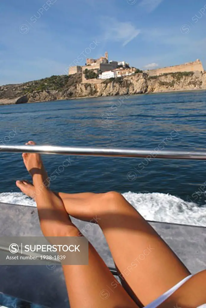 Legs of a young tanned woman  relaxed on a boat in Ibiza  with the castle and city walls in view
