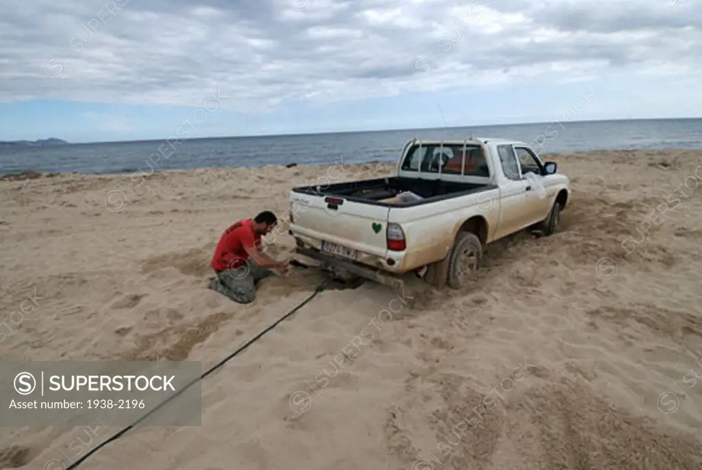 Young man trying to get his trapped pickup car out of the sand