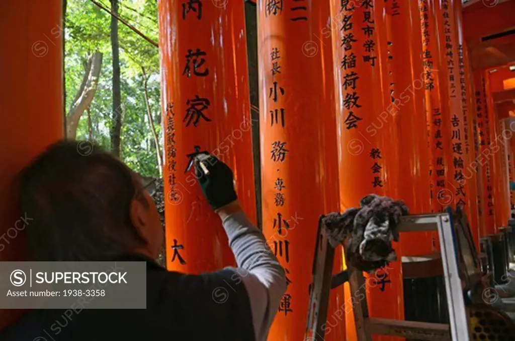 Restorer painting letters of a Torii gate at Fushimi Inari-Taisha shrine, Kyoto City, Honshu, Japan